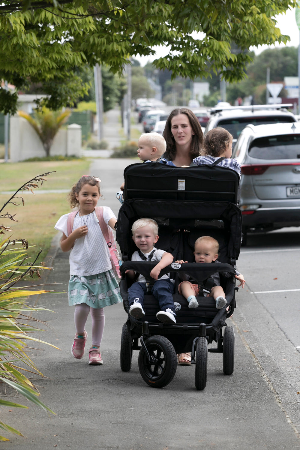 A childminder pushes a quad stroller with four children in a KinderPod in a real outdoor street environment.