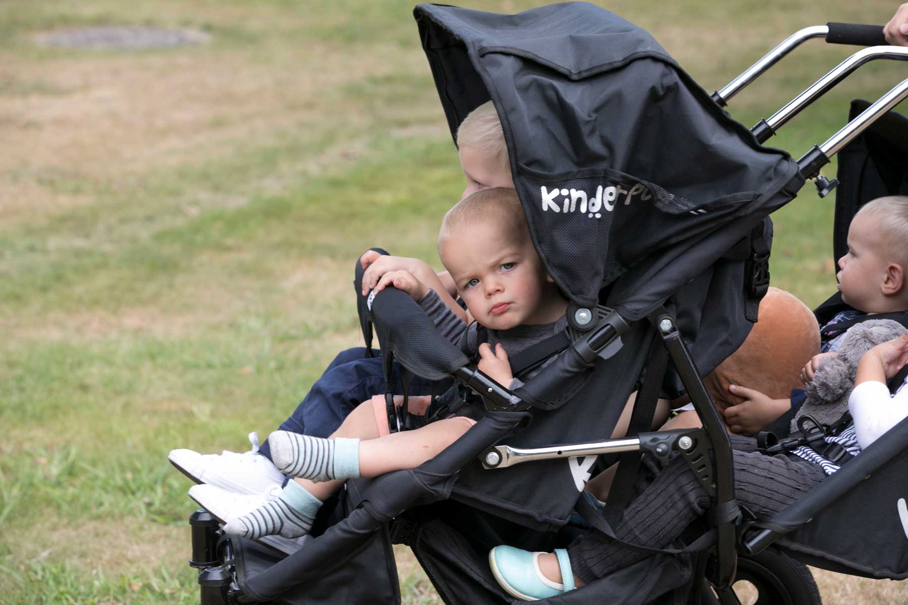 Four children in a KinderPod Four seat stroller with a rear double recliner baby seat attached.