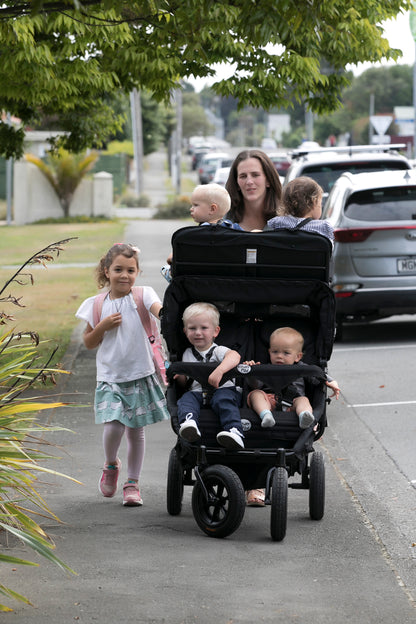 A childminder pushes a quad stroller with four children in a KinderPod in a real outdoor street environment. 