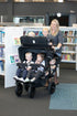 A multi-seat push chair with six children been pushed by a childminder in a library