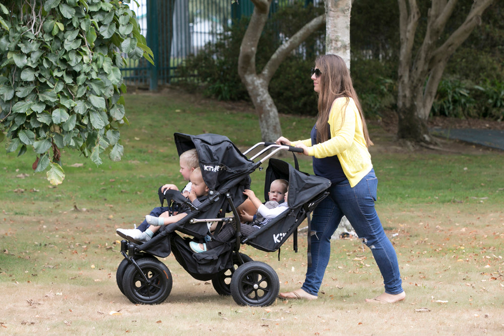 A multi-seat quad seat buggy been pushed by a childminder with four children at a park