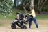 A multi-seat quad seat buggy been pushed by a childminder with four children at a park